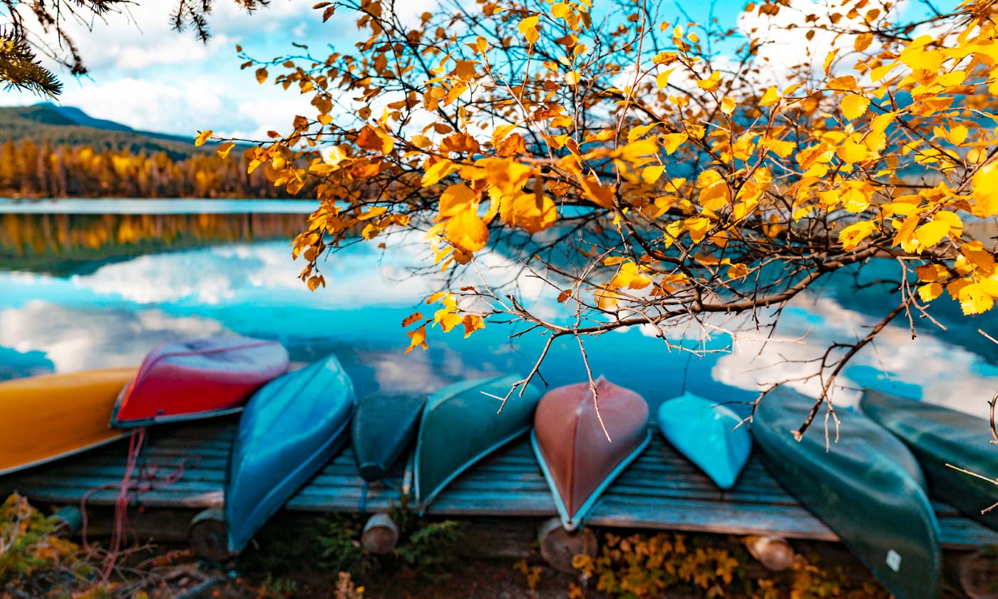 Row of canoes neatly stacked by beautiful lake surrounded by fall folliage